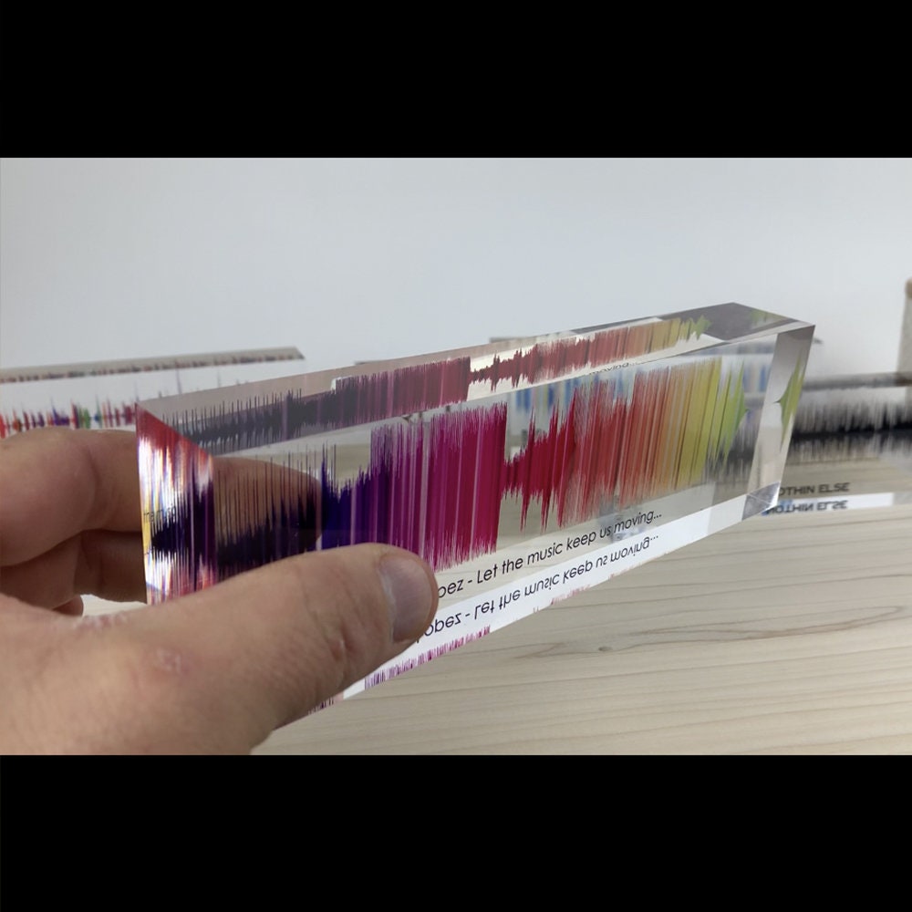 Colorful sound wave pattern in a clear block held by a hand.